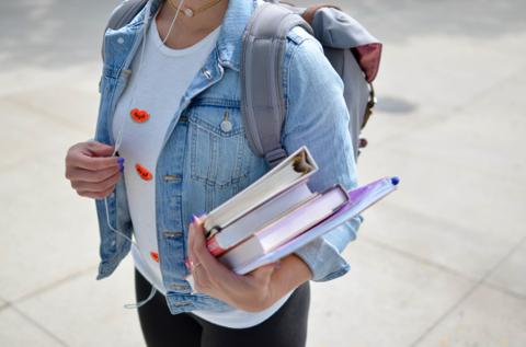 Student holding notebooks and backpack, walking to class.